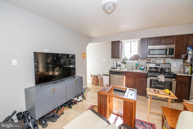 kitchen with dark brown cabinets, appliances with stainless steel finishes, light wood-type flooring, and sink