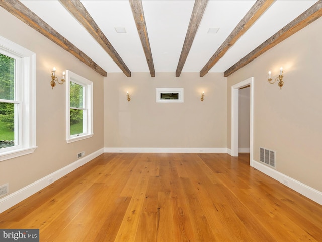 unfurnished room featuring beamed ceiling, a wealth of natural light, and wood-type flooring