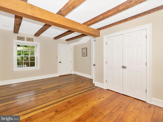 unfurnished bedroom featuring beamed ceiling and hardwood / wood-style floors