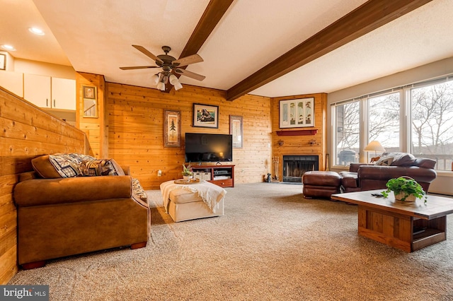 carpeted living room featuring beamed ceiling, a fireplace, wood walls, and ceiling fan