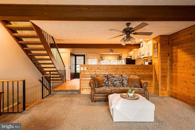 carpeted living room featuring wooden walls, ceiling fan, beamed ceiling, and a textured ceiling