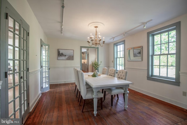 dining area with a notable chandelier, rail lighting, and dark wood-type flooring