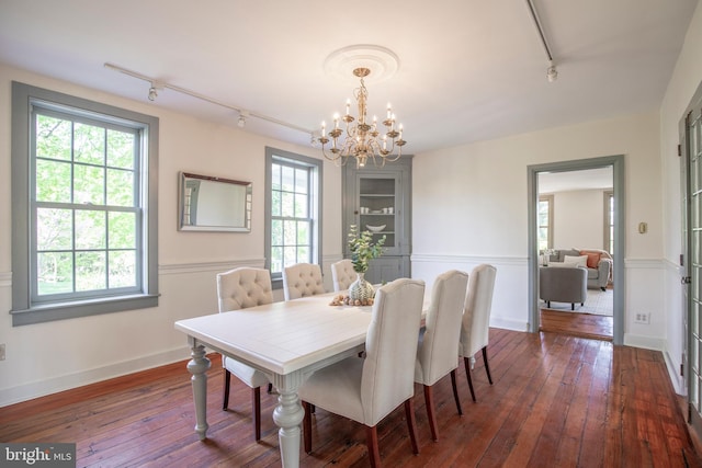 dining space with rail lighting, a healthy amount of sunlight, dark wood-type flooring, and a chandelier