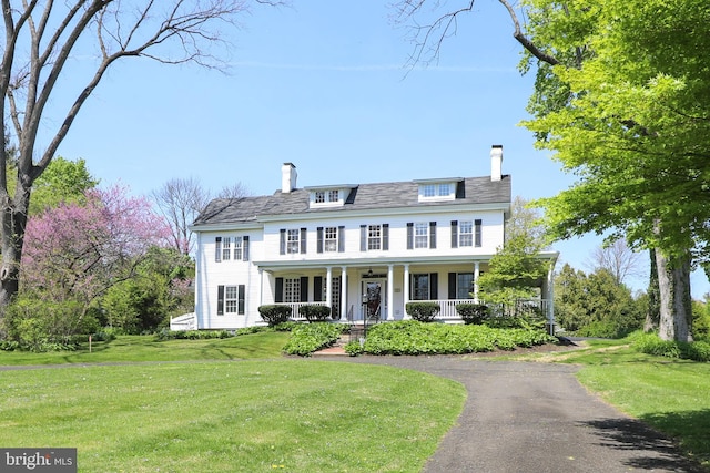 colonial home featuring covered porch and a front yard