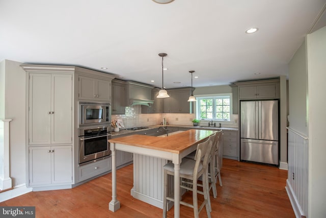 kitchen with stainless steel appliances, tasteful backsplash, wall chimney exhaust hood, hardwood / wood-style floors, and a center island