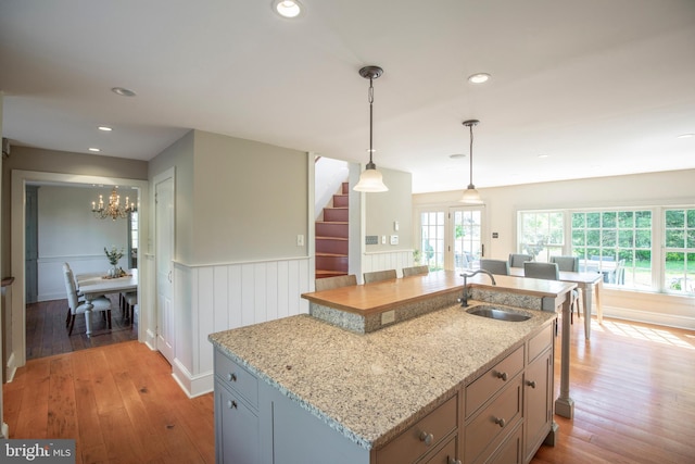kitchen with light hardwood / wood-style flooring, sink, decorative light fixtures, a center island with sink, and an inviting chandelier