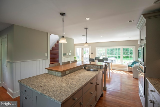 kitchen featuring sink, decorative light fixtures, stainless steel appliances, a center island with sink, and hardwood / wood-style flooring