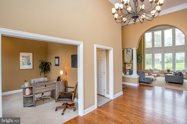 office area with a notable chandelier, a high ceiling, crown molding, decorative columns, and light hardwood / wood-style floors