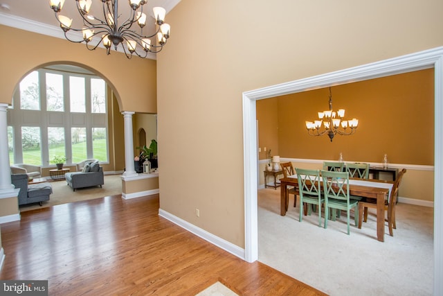 dining space featuring an inviting chandelier, crown molding, ornate columns, wood-type flooring, and a towering ceiling