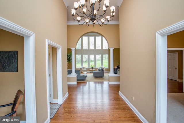 hall featuring a notable chandelier, hardwood / wood-style flooring, a high ceiling, ornamental molding, and decorative columns