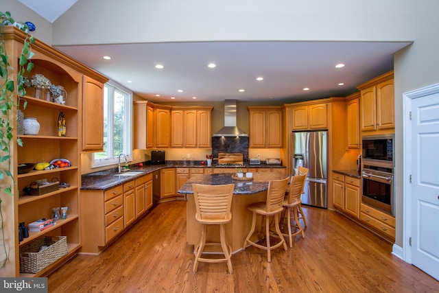 kitchen with a center island, wall chimney exhaust hood, appliances with stainless steel finishes, hardwood / wood-style flooring, and a kitchen bar