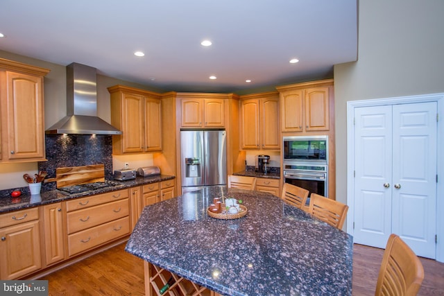 kitchen featuring appliances with stainless steel finishes, a center island, hardwood / wood-style floors, and wall chimney range hood