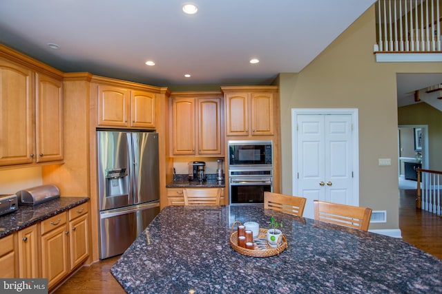 kitchen with appliances with stainless steel finishes, dark stone counters, dark hardwood / wood-style flooring, and a kitchen breakfast bar