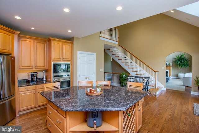 kitchen with dark stone countertops, light wood-type flooring, a center island, stainless steel appliances, and a towering ceiling