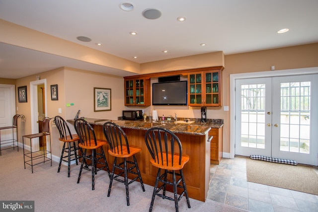 kitchen featuring french doors, kitchen peninsula, dark stone counters, light colored carpet, and a kitchen breakfast bar