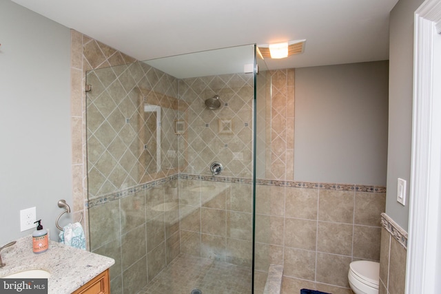 bathroom with a shower with shower door, vanity, tile walls, and toilet