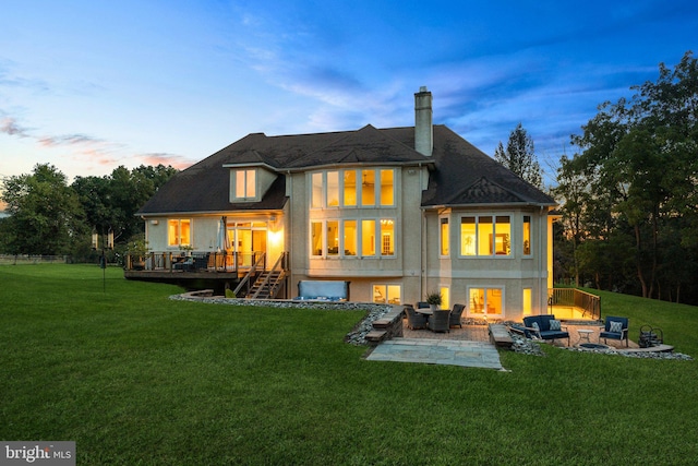 back house at dusk with an outdoor fire pit, a lawn, and a wooden deck