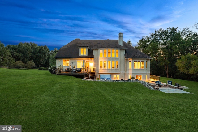 back house at dusk featuring a deck and a lawn