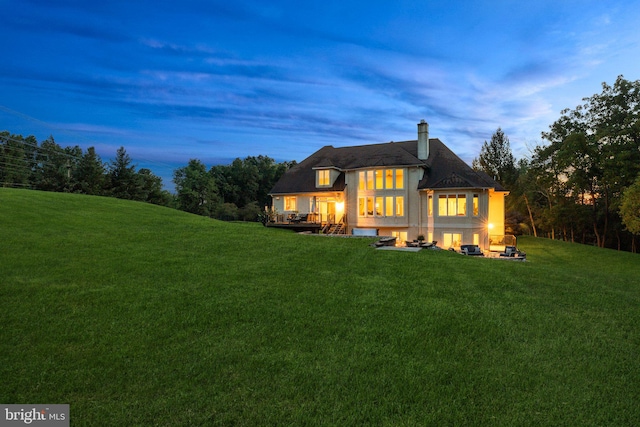 back house at dusk featuring a deck and a lawn