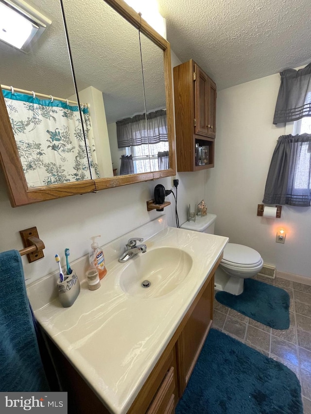 bathroom featuring tile flooring, vanity, toilet, and a textured ceiling