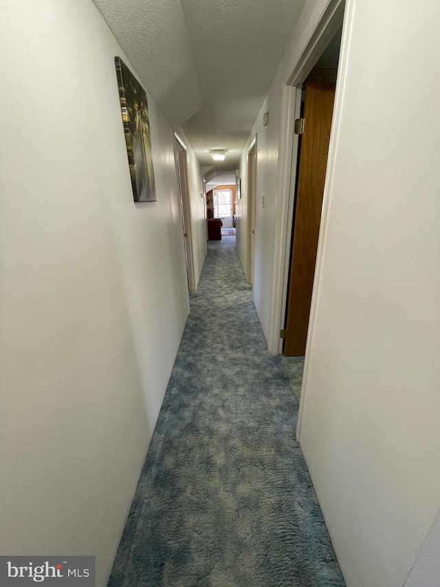 corridor featuring a textured ceiling and dark colored carpet