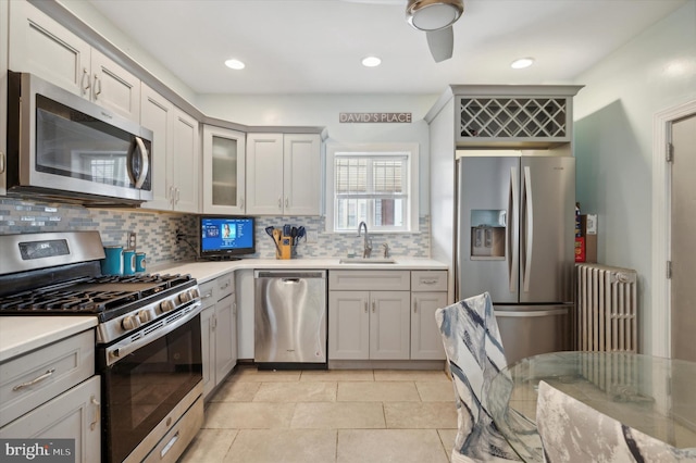 kitchen with radiator, appliances with stainless steel finishes, backsplash, light tile flooring, and sink