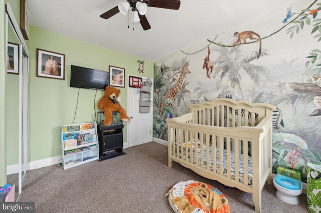 bedroom with dark carpet, ceiling fan, and a crib