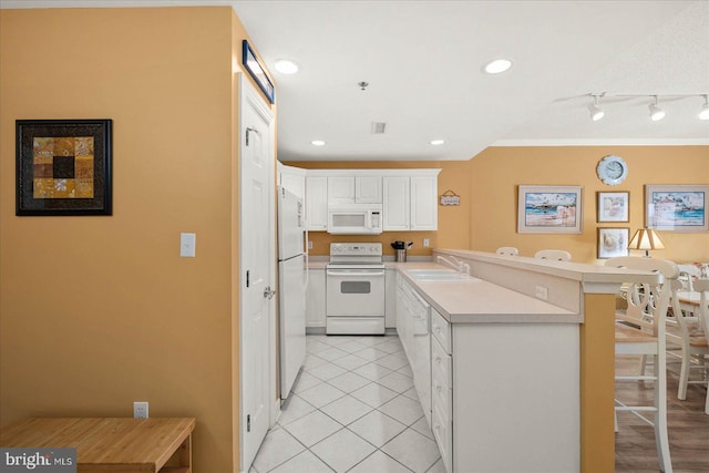 kitchen featuring white appliances, white cabinetry, sink, a breakfast bar area, and track lighting