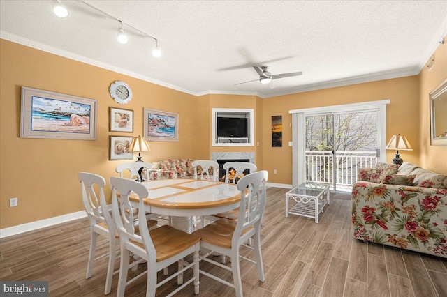 dining room with ceiling fan, a textured ceiling, rail lighting, hardwood / wood-style floors, and ornamental molding