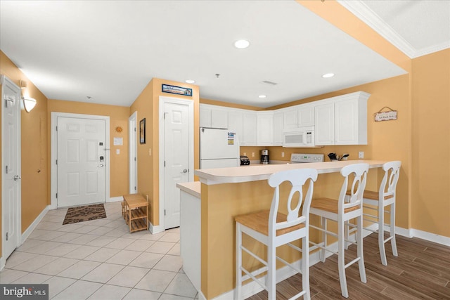 kitchen with kitchen peninsula, a kitchen bar, white appliances, crown molding, and white cabinets