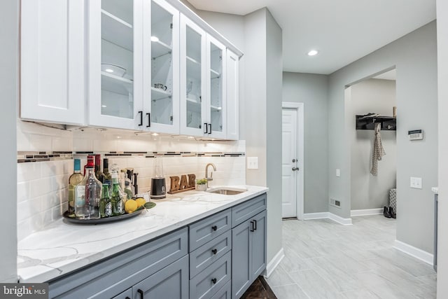 bar featuring white cabinets, sink, backsplash, and light tile flooring