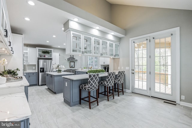 kitchen featuring a kitchen island, a breakfast bar, white cabinets, plenty of natural light, and stainless steel refrigerator with ice dispenser