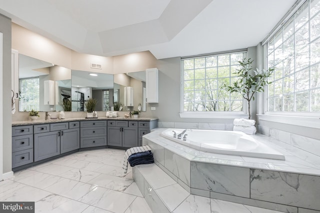 bathroom with a healthy amount of sunlight, a relaxing tiled bath, vanity, and tile floors