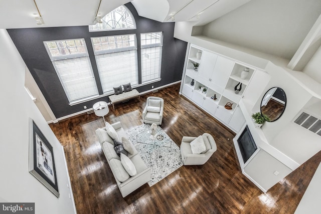 living room featuring built in features, dark wood-type flooring, track lighting, and a high ceiling