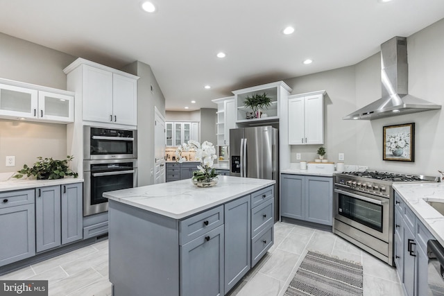 kitchen with stainless steel appliances, wall chimney range hood, light tile floors, and white cabinetry