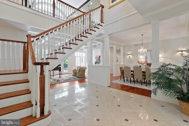 tiled foyer with an inviting chandelier, ornate columns, crown molding, and a high ceiling