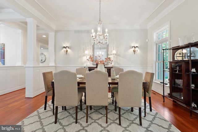 dining room featuring decorative columns, light hardwood / wood-style flooring, crown molding, and a chandelier