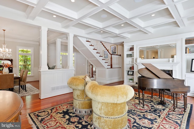 living area featuring wood-type flooring, a fireplace, a notable chandelier, and decorative columns