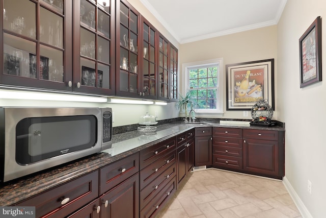 kitchen with ornamental molding, sink, light tile floors, and dark stone counters