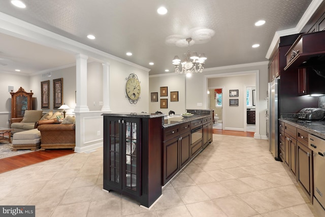 kitchen featuring ornamental molding, light tile flooring, ornate columns, and a kitchen island with sink