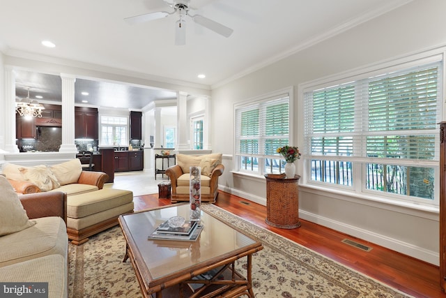 living room with light hardwood / wood-style floors, decorative columns, ceiling fan with notable chandelier, sink, and ornamental molding