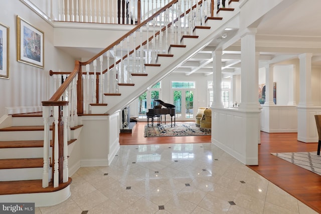 staircase with ornate columns, a towering ceiling, light tile floors, and ornamental molding