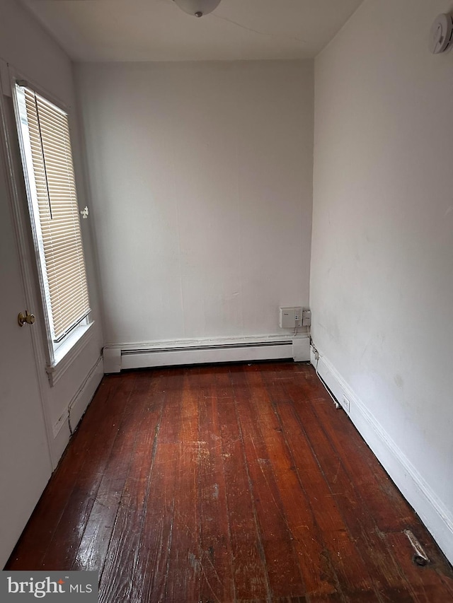 unfurnished room featuring a baseboard heating unit and dark hardwood / wood-style floors