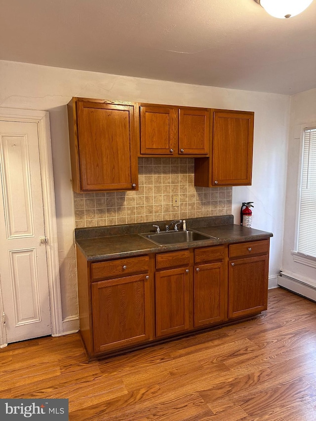 kitchen with a baseboard heating unit, sink, light hardwood / wood-style floors, and decorative backsplash