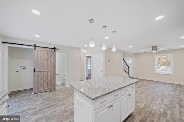 kitchen featuring decorative light fixtures, white cabinets, a barn door, a center island, and light stone countertops