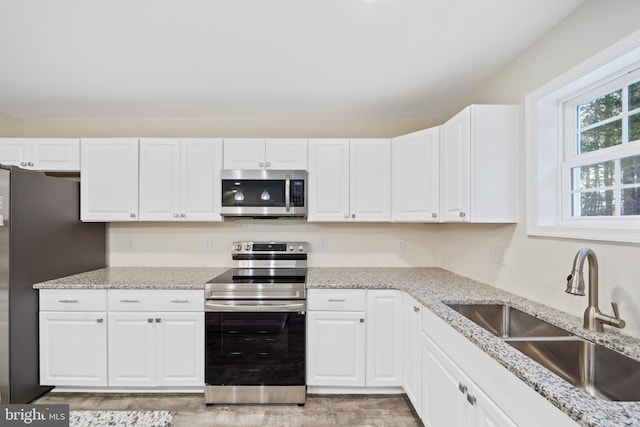 kitchen with sink, light stone countertops, white cabinets, and appliances with stainless steel finishes