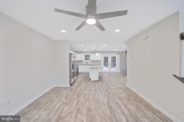 unfurnished living room featuring a barn door, ceiling fan, and light wood-type flooring