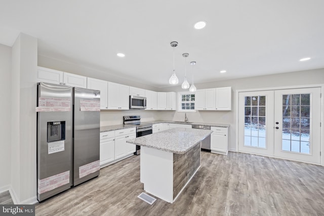 kitchen featuring a kitchen island, appliances with stainless steel finishes, decorative light fixtures, sink, and white cabinets