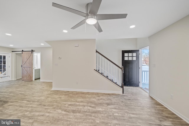 unfurnished living room featuring ceiling fan, a barn door, and light hardwood / wood-style floors