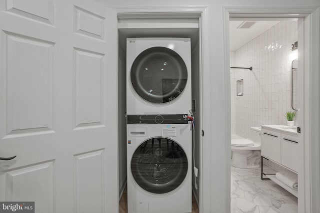 clothes washing area with stacked washer and clothes dryer and light tile floors